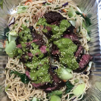 A tray of noodles with meat and vegetables on top